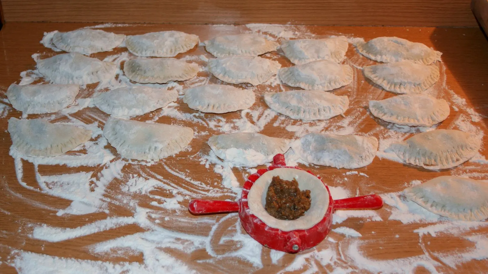 Ulepione pierogi na stolnicy posypanej mąką i miseczka z farszem