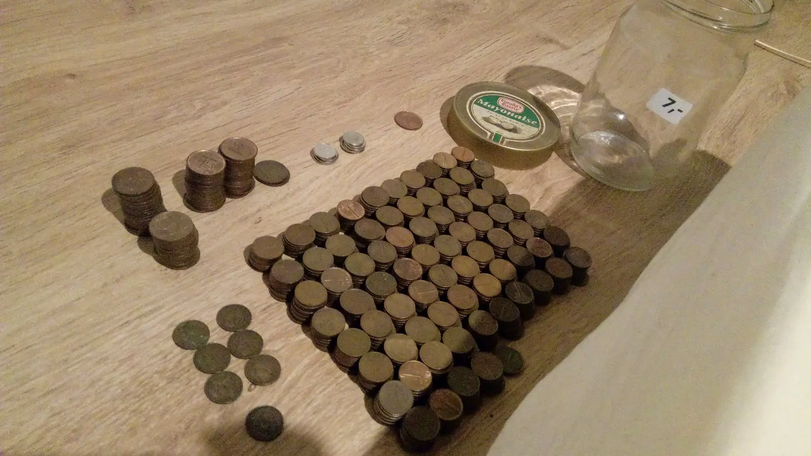 Stosy monet ułożone na drewnianym stole obok słoika na oszczędności